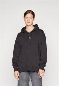 Felpa nera con cappuccio realizzata in cotone misto, con maniche lunghe, tasca frontale, cappuccio con lacci e un piccolo logo sul petto.
