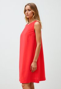 Abito rosso senza maniche, silhouette A-line rilassata, tessuto liscio, lunghezza al ginocchio, con scollatura rotonda e dettagli di tasche laterali sottili.