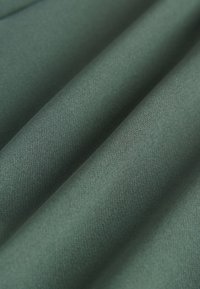 Soft, folded green fabric with a smooth, tightly woven texture and subtle shading highlighting the creases.