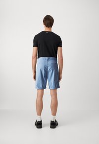 Blå bomullsshorts med rulleopplegg, med baklommer, kombinert med en svart kortermet skjorte og svarte joggesko. Minimalistisk design.