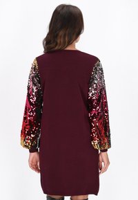 Bordó ruha hosszú ujjal, sokszínű flitterekkel piros, rózsaszín, arany és fekete árnyalatokban. Simább textúrájú és térdig érő fazonú.
