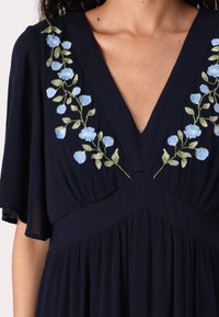 Navy dress with a deep V-neck, featuring blue floral embroidery along the neckline and soft, flowing fabric with a gathered waist.