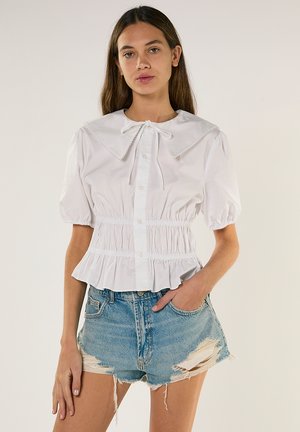 Hvid bluse med pufærmer, stor krave, indsnøret talje og knapper foran. Bæres med slidte denimshorts med frynsete kanter.