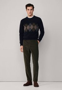 Marineblå sweater med rombemønster i brun og grøn, kombineret med mørkegrønne bukser og brune ankelstøvler. Glat stof, tætsiddende design.