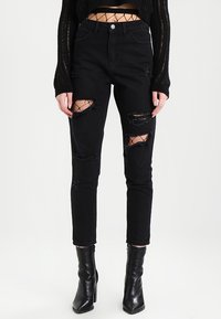 Černé skinny džíny s roztržením na kolenou, vyrobené z denimu. Nosí se s černými kotníkovými botami a černým zkráceným svetr s síťovými detaily.