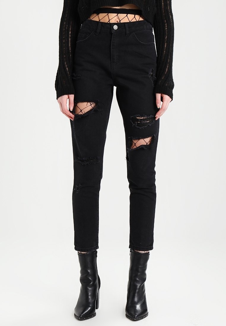 Černé skinny džíny s roztržením na kolenou, vyrobené z denimu. Nosí se s černými kotníkovými botami a černým zkráceným svetr s síťovými detaily.