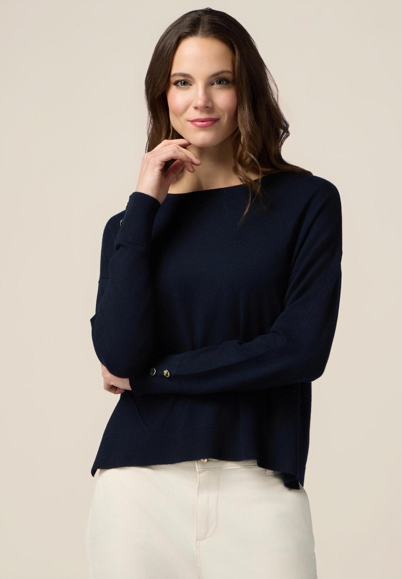 Niebieski sweter dzianinowy z szerokim dekoltem, opuszczonymi ramionami i złotymi guzikami na rękawach. Miękka struktura; luźny krój.