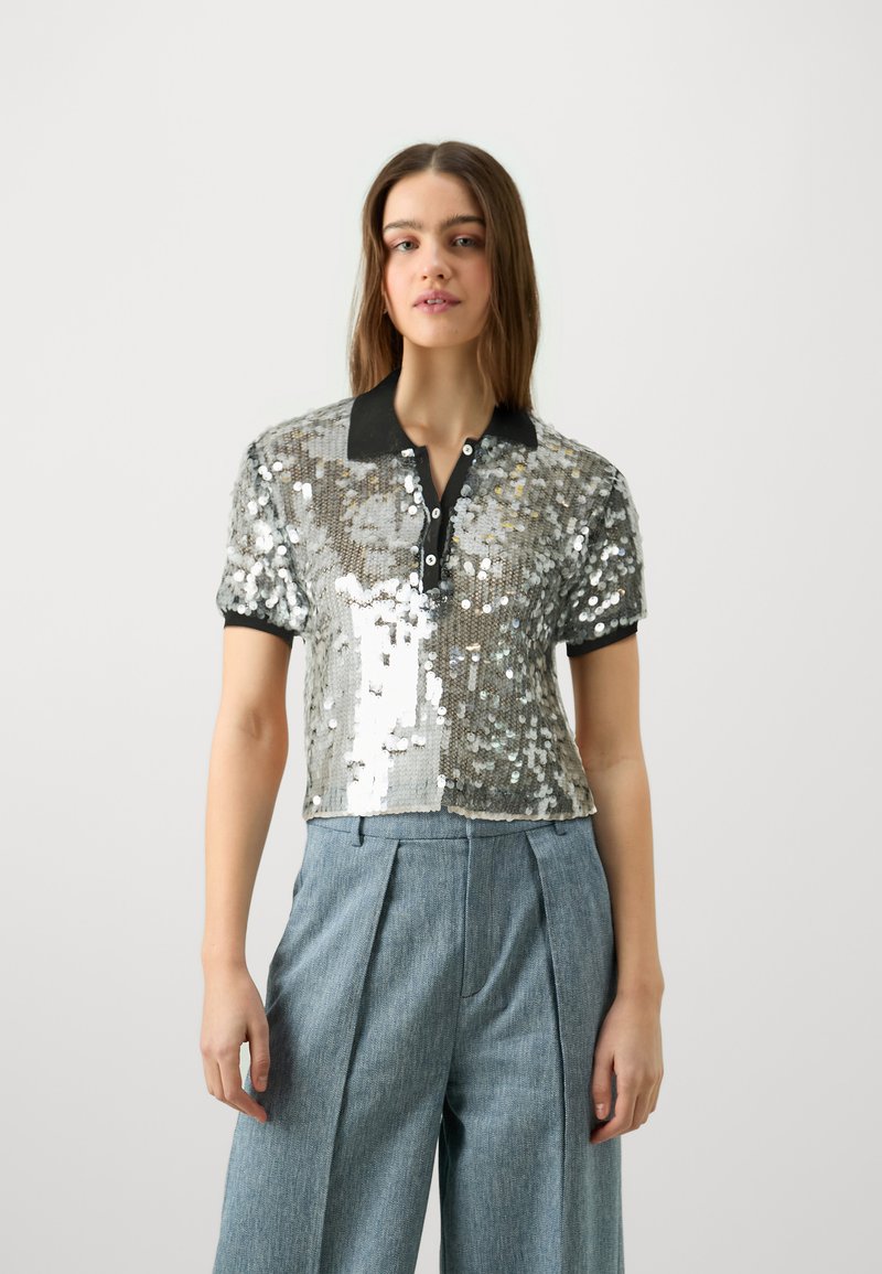 Polo corto ricoperto di paillettes argentate con colletto e bottoni neri. Abbinato a pantaloni in denim chiaro a vita alta.