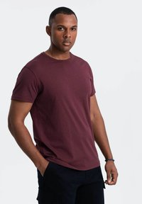Burgunderfarbendes Rundhals-T-Shirt aus Baumwolle mit kurzen Ärmeln, taillierter Form und glatter Textur. Getragen mit schwarzen Cargo-Shorts.