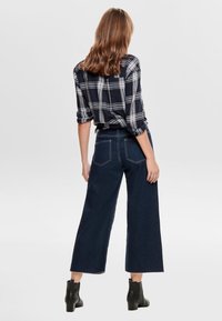 Rutig svart och vit skjorta med rullade ärmar, i kombination med vida mörkblå jeans och ankelstövlar, sedd från baksidan.