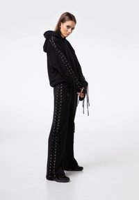 Czarny komplet z bluzą i spodniami z detalami sznurowania po bokach, wykonany z gładkiego materiału o luźnym kroju i regulowanymi sznurkami.