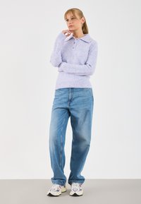 Pullover lavanda a maglia con colletto e tre bottoni, abbinato a jeans in denim blu chiaro a gamba dritta e sneakers multicolori.