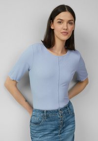 Jasnoniebieski prążkowany top z krótkimi, rozkloszowanymi rękawami i okrągłym dekoltem, w połączeniu z dżinsową spódnicą z przodu zapinaną na guziki i kieszeniami.