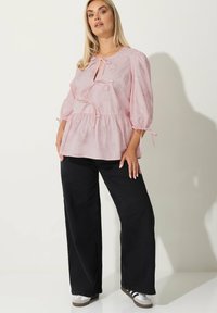 Top peplum rosa con scollo a chiave, maniche lunghe a sbuffo e dettagli con fiocco, caratterizzato da un motivo floreale. Abbinato a pantaloni neri a gamba larga.