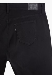 Svarte denimjeans med en strukturert overflate, med en baklomme som har et karakteristisk buet stikningsmønster og en merkelapp på livet.