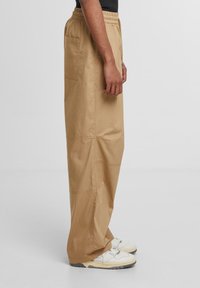 Beige, loose-fitting trousers with an elastic waist, side pockets, and subtle stitching details. Paired with white sneakers.