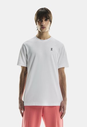 Tricou alb din bumbac, cu guler rotund și mâneci scurte, având un mic logo negru în zona stângă a pieptului.