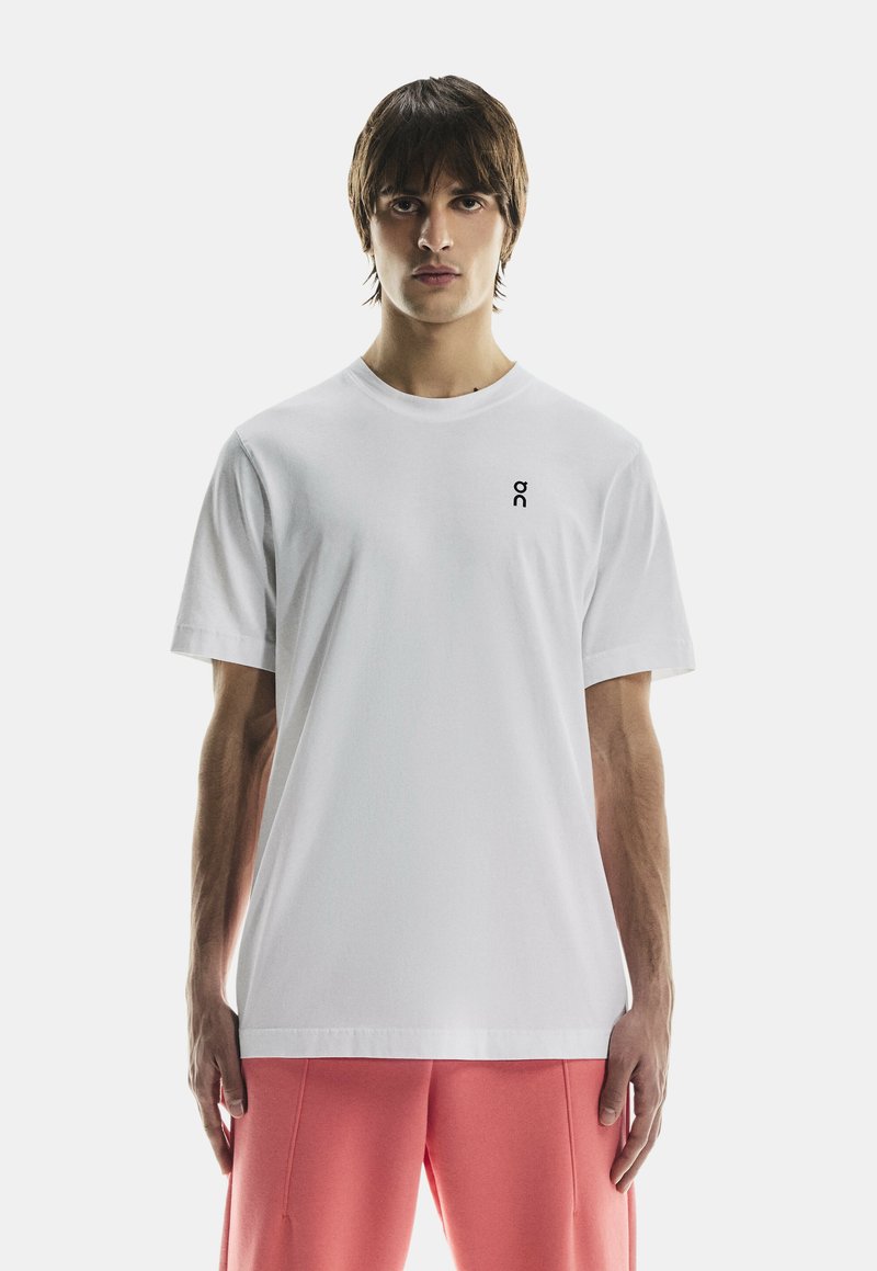 Vit bomulls-t-shirt med rund hals och korta ärmar, med en liten svart logotyp på vänster bröst.