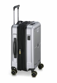 Valigia rigida argento con compartimento zip nero, manico retrattile e quattro ruote con accenti gialli per la mobilità.