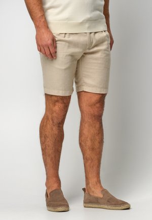 Shorts di lino beige con una vestibilità comoda, orli risvoltati e una cintura elastica confortevole, abbinati a scarpe slip-on marroni.