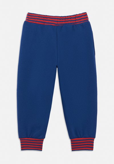 Detské modré teplákové nohavice s elastickým pásom a manžetami, ktoré majú červené a modré horizontálne pruhy.
