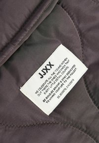 Tejido de color púrpura oscuro con una textura acolchada presenta una etiqueta blanca que muestra texto y un logo, cosida en el borde.