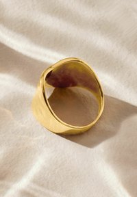 Goldene Metallring mit einem glatten, geschwungenen Design und einer polierten Oberfläche, ausgestattet mit einem nahtlosen Band und einer sanften, organischen Form.