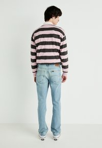 Camisa de manga larga a rayas en rosa y gris, combinada con jeans azul claro. La camisa presenta un collar blanco, lo que añade contraste al diseño.