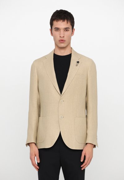 Beige Leinenblazer mit zwei Knöpfen, Reverskragen und zwei Fronttaschen. Mit einer dekorativen schwarzen Nadel am linken Revers.