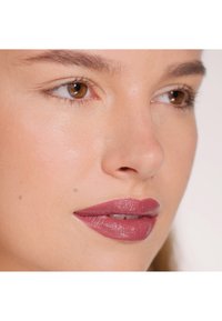 Matte mauve lipstick on smooth lips, with natural skin texture and warm brown eyes. Subtle gloss accentuates lip shape.