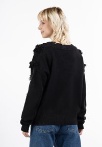 Zwarte, textuurtrui met een ronde hals, voorzien van franjes op de schouders. Gepaard met hoge blauwe denim jeans.