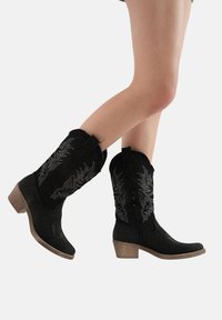 Czarne kowbojskie buty z dekoracyjnym szarym haftem, wykonane z materiału przypominającego filc, z zaokrąglonym noskiem i niskim, solidnym obcasem.