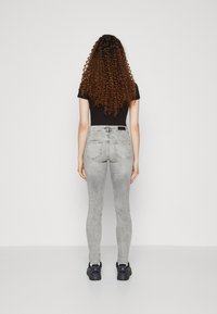 Jeans ajustados grises con un lavado desvaído, cintura alta y bolsillos traseros. Combinados con una blusa negra ajustada y zapatos negros. Pelo largo y rizado.