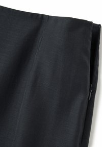 Gros plan sur un vêtement en tissu noir montrant la couture latérale et la fermeture éclair noire partiellement ouverte.