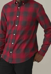 Camisa de franela a cuadros en rojo y negro con diseño de botones, mangas largas, un bolsillo en el pecho y un acabado de tela texturizada.