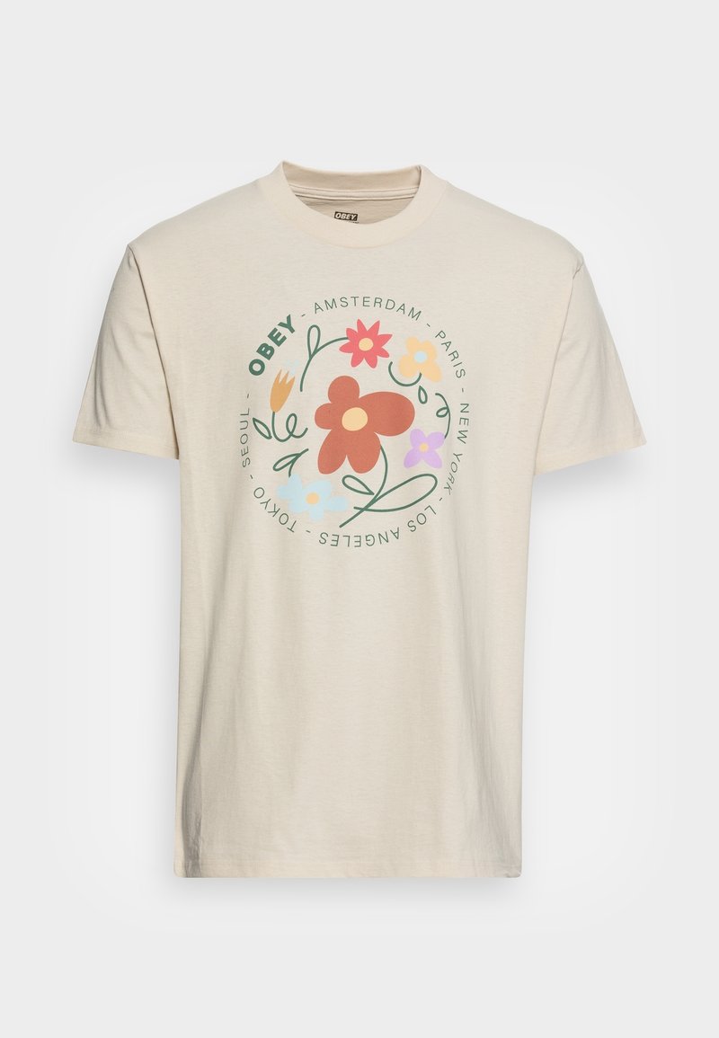 T-shirt en coton beige à manches courtes, présentant un graphique floral coloré et des noms de villes disposés en motif circulaire sur le devant.