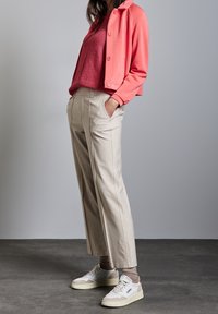 Ljus korallfärgad kort jacka, texturerad vinröd tröja, skräddarsydda beige byxor och vita sneakers med neutrala accenter. Slätt, strukturerat tyg.