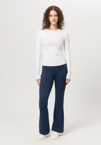 Top blanco de manga larga con panel texturizado y pantalones acampanados azul marino, ambos hechos de una tela suave y elástica, combinados con deportivas blancas.