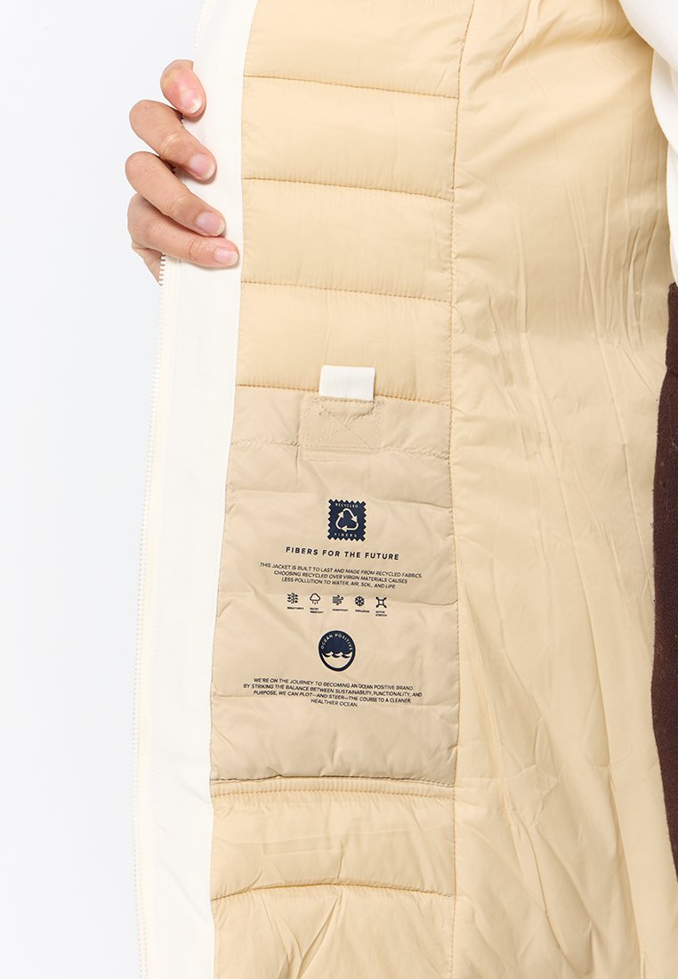 Giacca isolante con interno beige ed esterno bianco, dotata di un'etichetta riguardante materiali sostenibili e istruzioni per la cura.