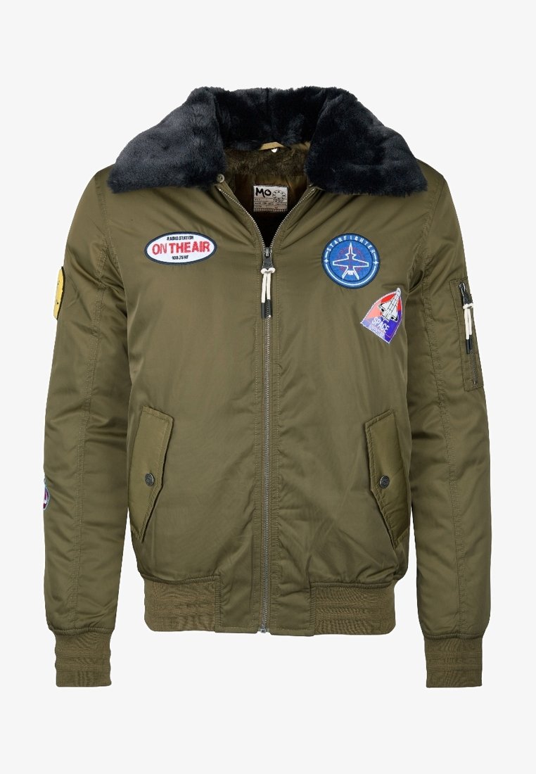 Veste bomber verte avec col en fourrure noire, fermeture éclair frontale, deux poches à rabat et patchs à thème spatial sur la poitrine et les manches.