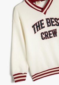 Felpa crema con polsini e collo a coste bianchi e bordeaux. "THE BEST CREW" ricamato in teal scuro e bordeaux.