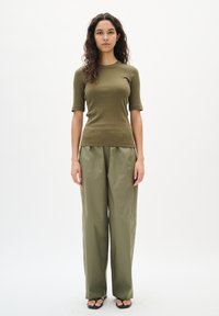 Olivgrünes, ribbed kurzärmliges Oberteil kombiniert mit lockeren olivgrünen Hosen aus leichtem Stoff, dazu minimalistische schwarze Sandalen.