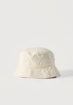 Pălărie de tip bucket din bumbac crem, cu cusături subtile și un logo mic brodat pe lateral, pe un fundal simplu, deschis la culoare.