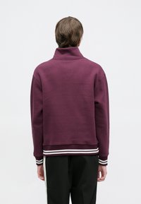 Bordeauxrode sweatshirt met een hoge kraag, ribgebreide manchetten en zoom met witte strepen. Zachte textuur, losse pasvorm, minimalistisch ontwerp.