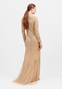 Beaded avonjurk in nude, met lange mouwen, een getailleerde silhoutte en een uitlopende onderkant. Intricate kraalwerk creëert een bloemontwerp patroon.