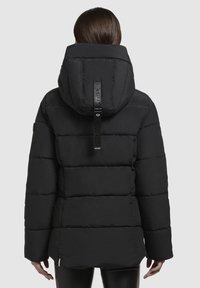 Doudoune noire avec capuche, présentant un design matelassé linéaire et une étiquette logo au dos. Texture lisse et manches longues.