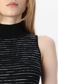 Fekete ujja nélküli felső, magas bordás nyakkivágással, váltakozó fekete és fehér vízszintes csíkokkal, valamint texturált kötött anyagból készült.