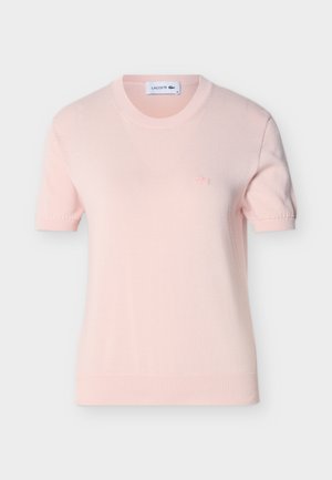 Haut tricoté à manches courtes rose clair avec encolure ronde et petit logo brodé sur le côté gauche de la poitrine, présenté sur un fond blanc.