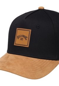 Gorra negra con visor de ante color coñac y un parche cuadrado de cuero marrón que presenta el logo de Billabong. Costuras visibles a lo largo del borde del visor.