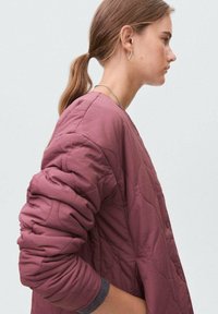 Prošívaná bunda v tlumené fialové barvě, s volným střihem, dlouhými rukávy a texturovaným povrchem se jemnými prošívacími detaily.